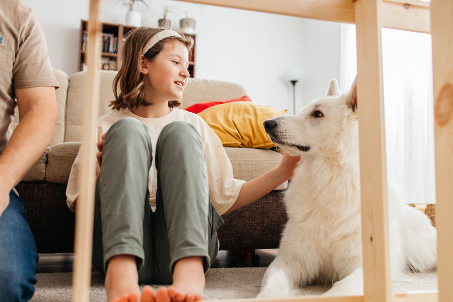 girl pets her dog on a living room floor