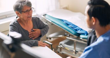 An older woman speaks with a healthcare provider while holding her chest during a medical visit.