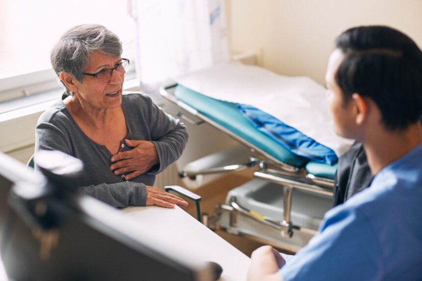 An older woman speaks with a healthcare provider while holding her chest during a medical visit.